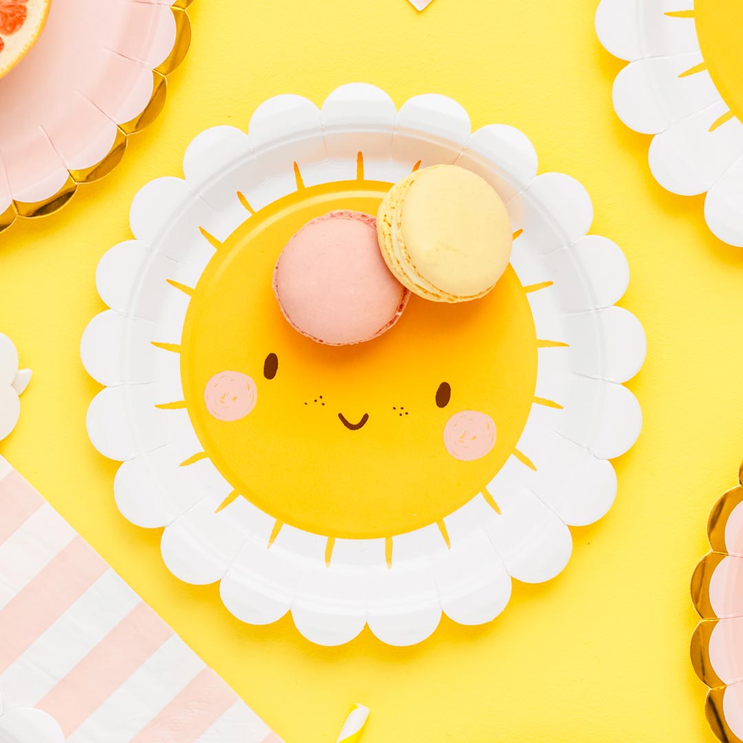Mesa de fiesta de verano decorada con platos de papel sol sonriente amarillo y blanco