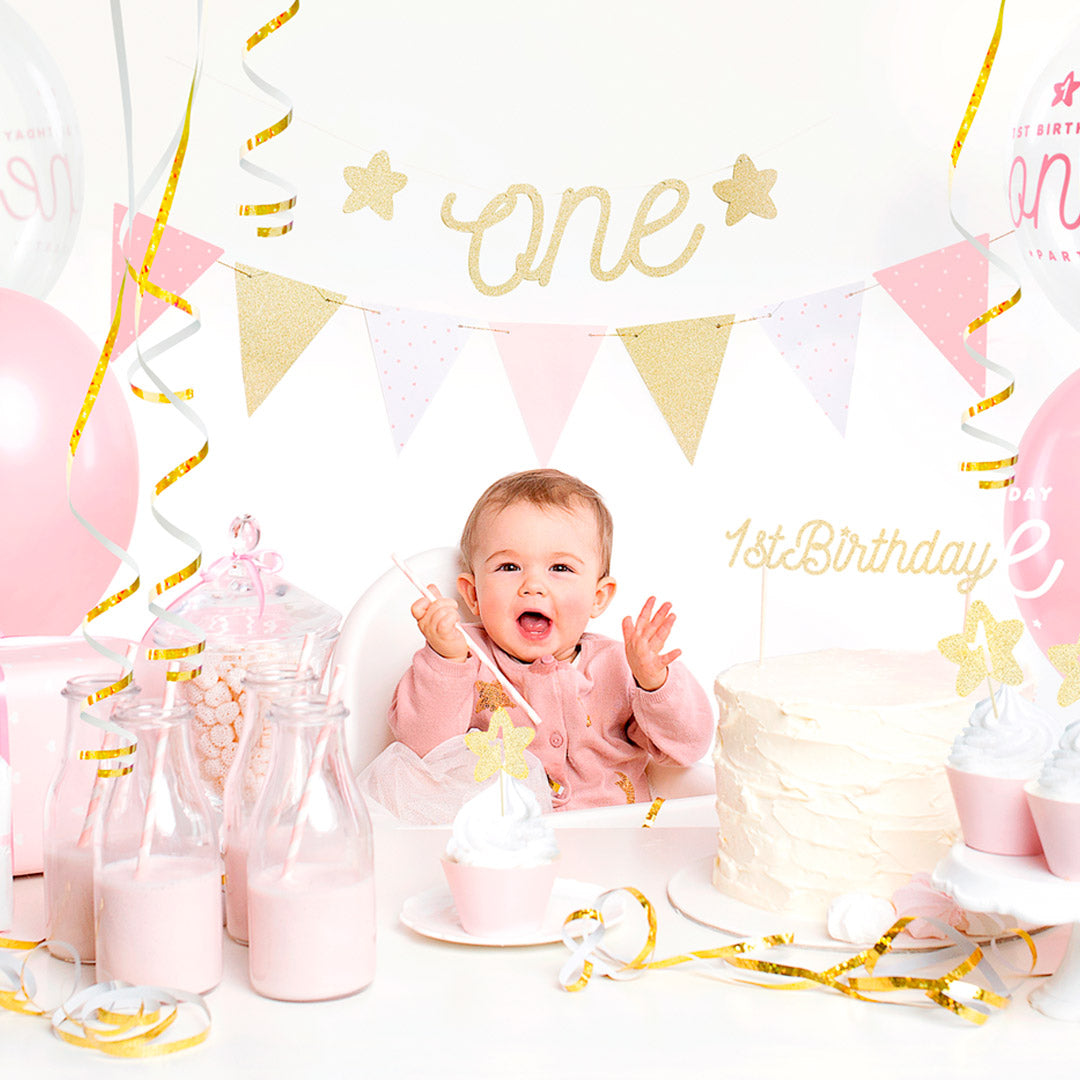 Set de decoraciones para primer cumpleaños en rosa y dorado con globos, guirnalda y toppers.