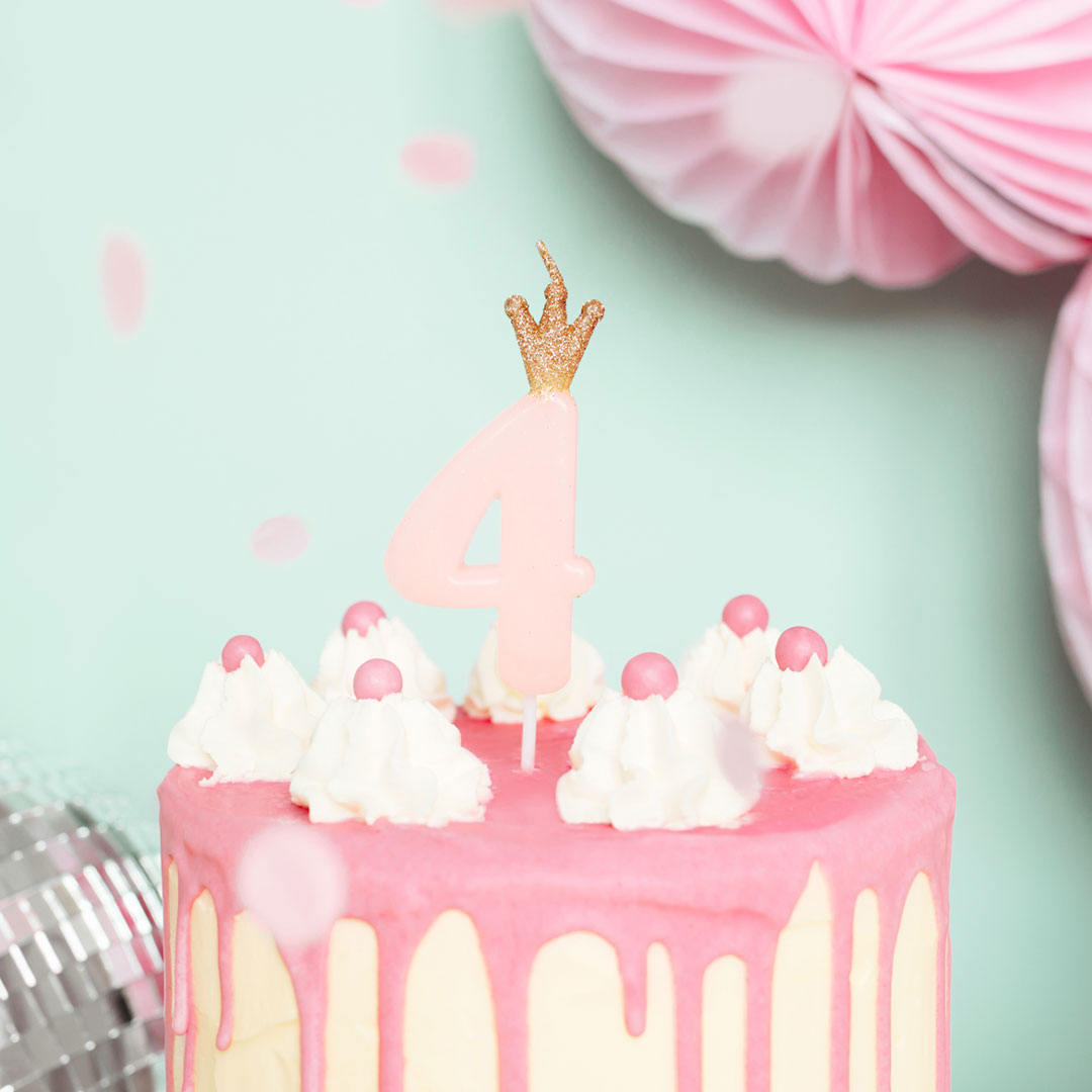 Vela de cumpleaños con número rosa y corona dorada decorando tarta de cumpleaños infantil